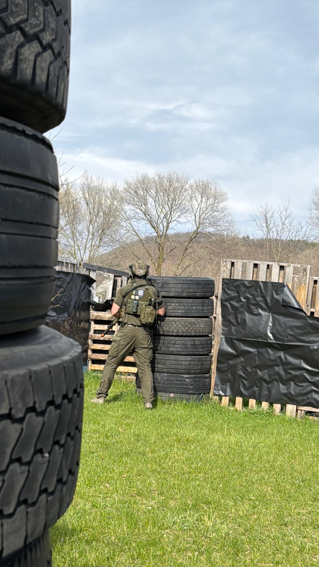 A player seen from behind in green tactical gear takes cover behind a tall stack of tyres on the Korhaven field