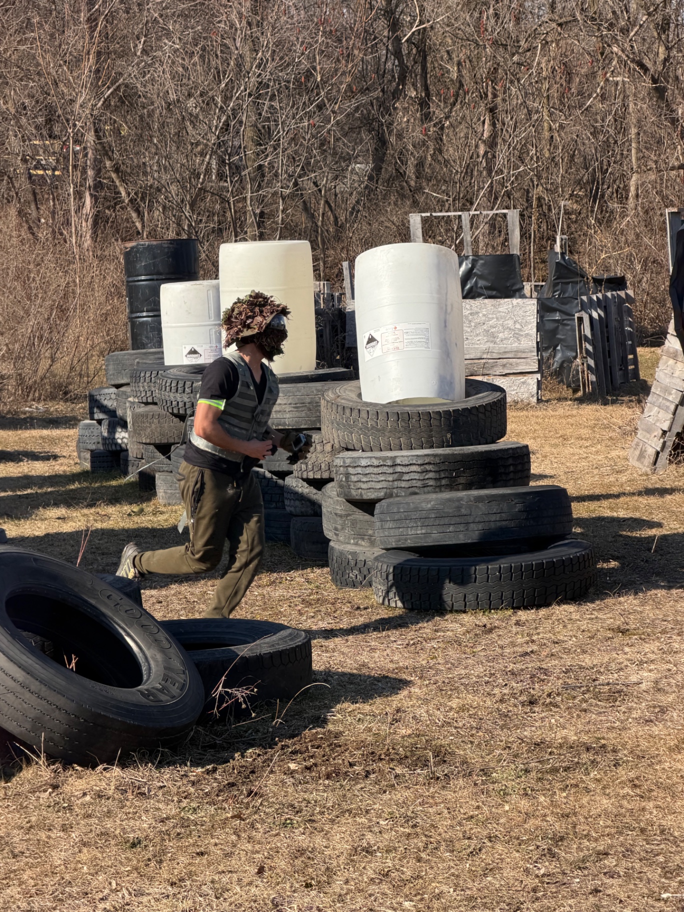 A player in tactical gear runs past tyre and barrel obstacles on the Korhaven field