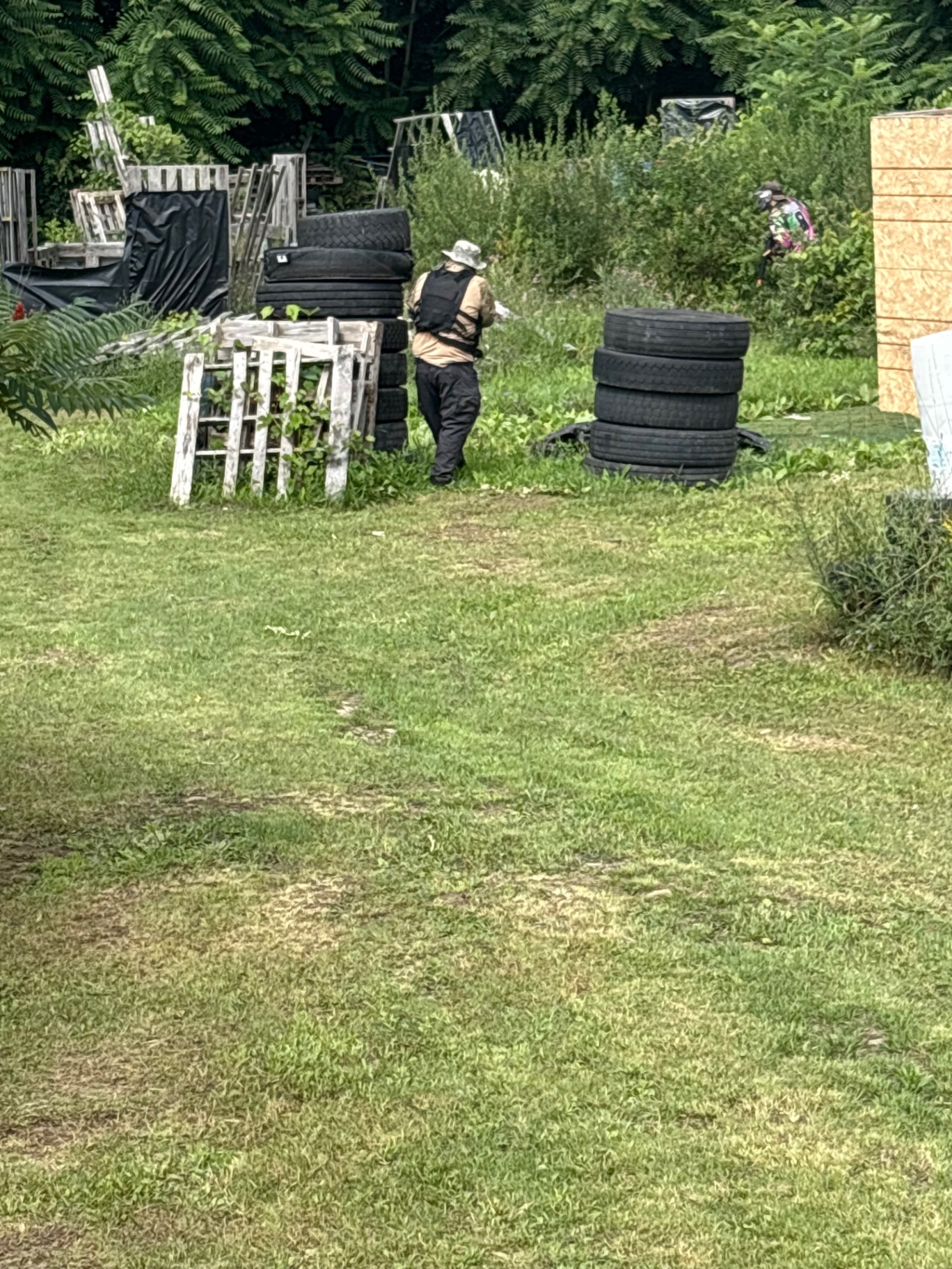 Players spread across the Korhaven field behind stacked tyre barricades, wooden pallets and a plywood wall, with dense trees beyond